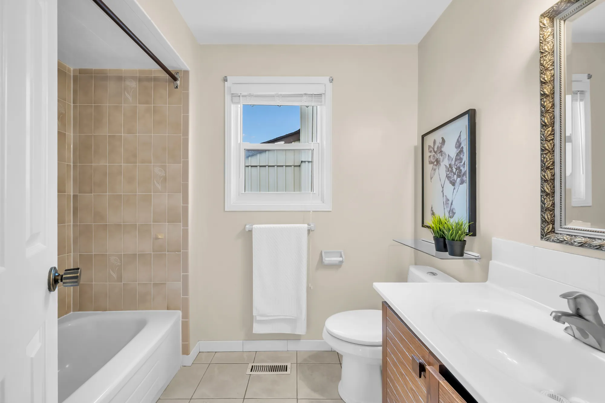 The second bathroom: a tub with a beige tiled surround, a toilet, a white vanity on a wood cabinet, a window