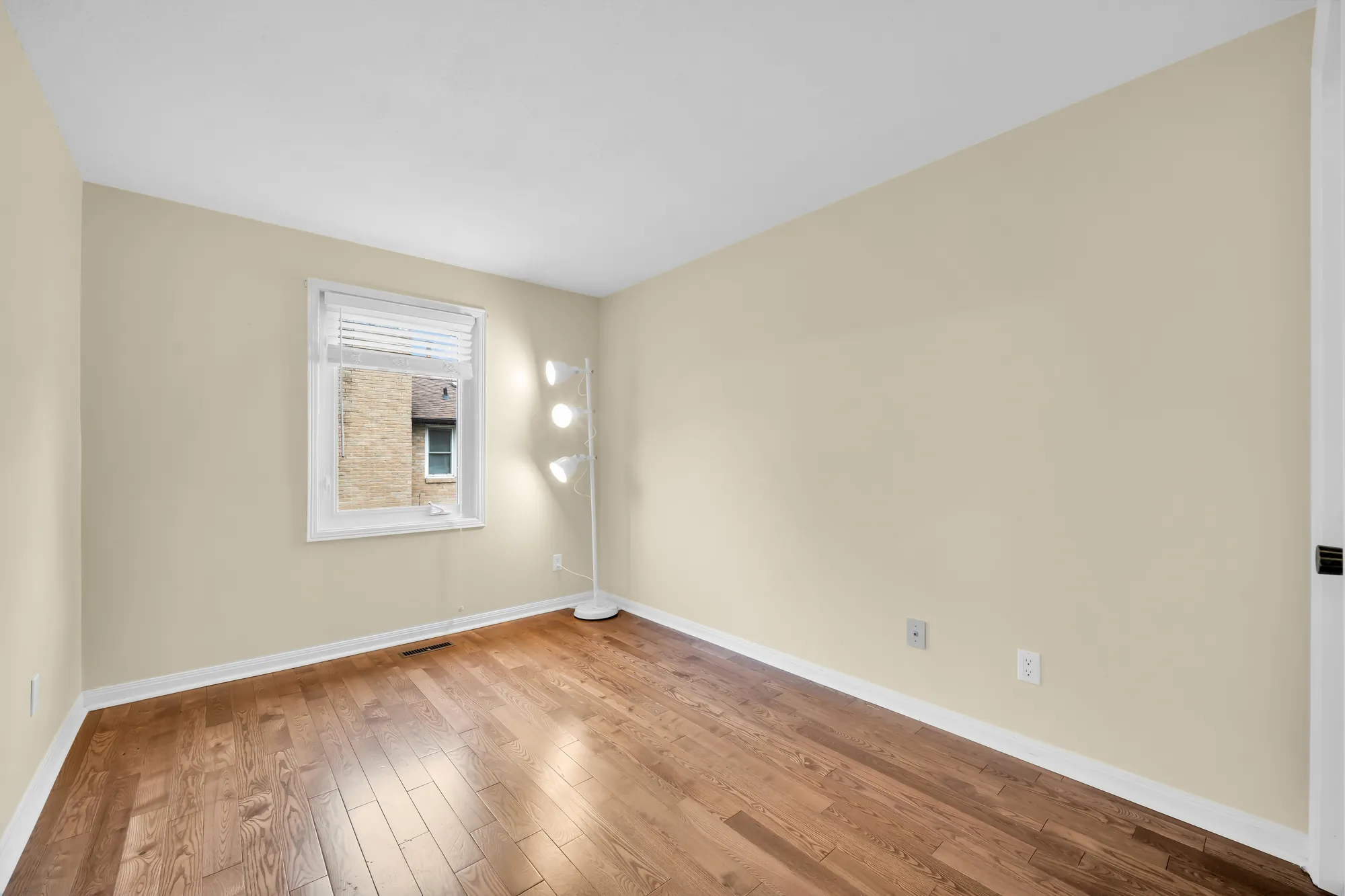 A bedroom with pale yellow walls, empty: a window with a blind, wood floors, a floor lamp in the corner
