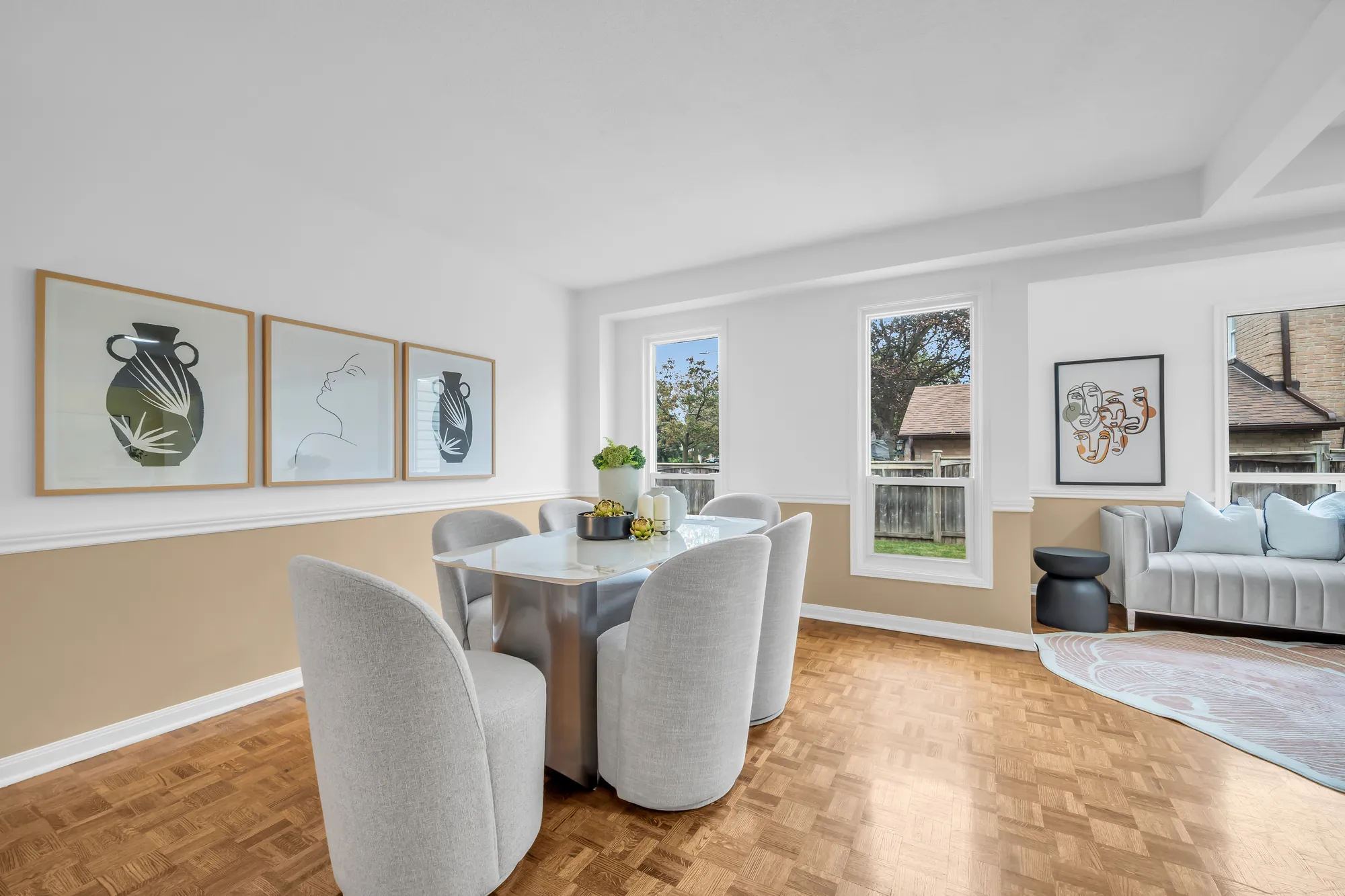 The dining area: a stone-topped table and four upholstered chairs, three framed prints, windows onto the back yard, a sofa beyond