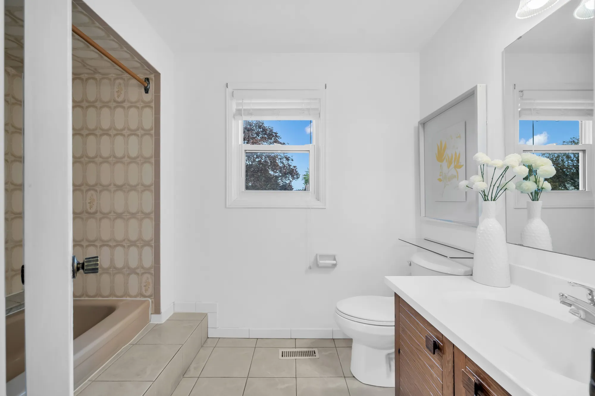 The primary bathroom: a tub with a patterned tile surround, a toilet, a white vanity on a wood cabinet, a window