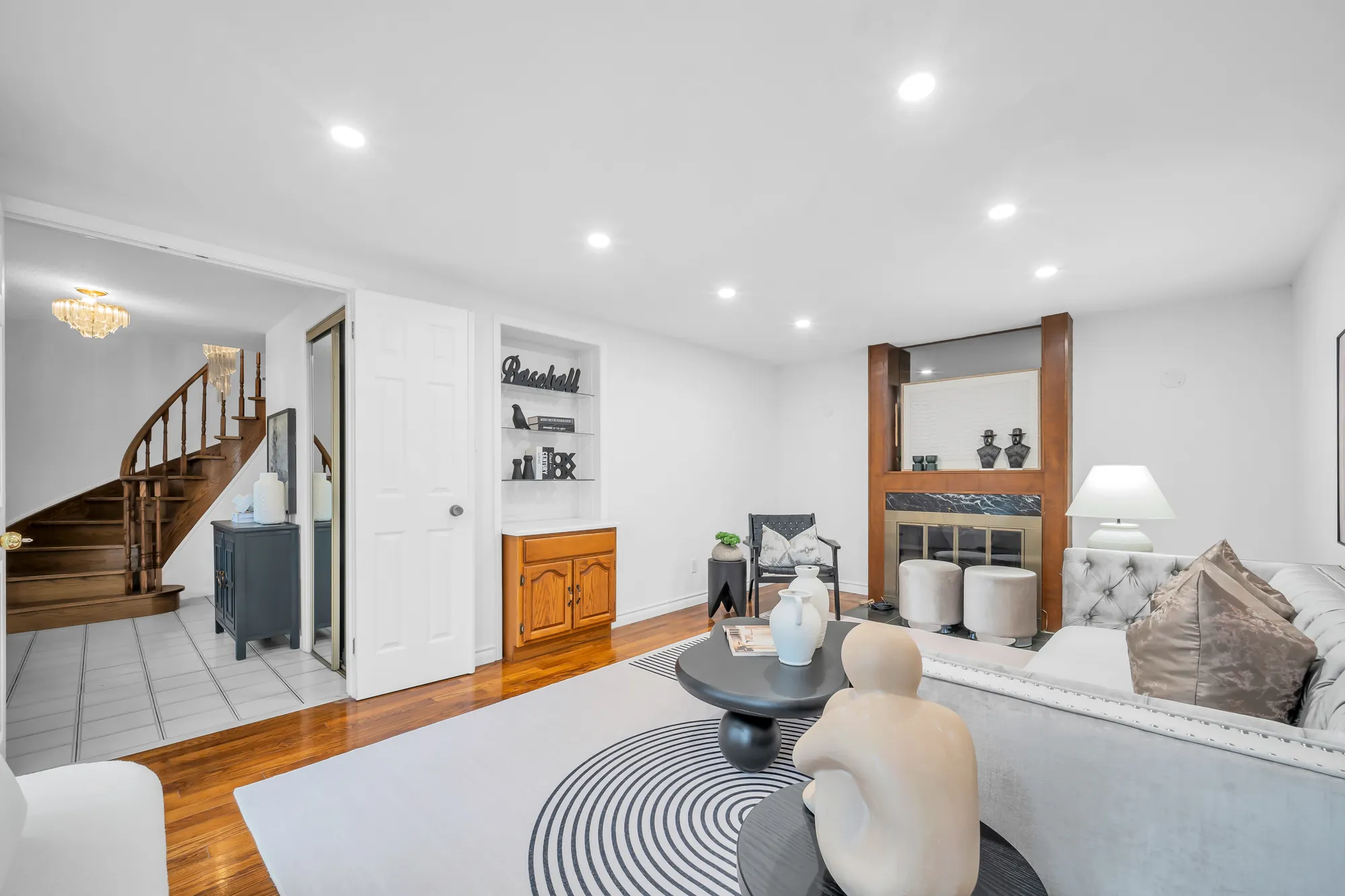 The family room toward the foyer: the curved staircase through the doorway, the fireplace and the built-in shelf