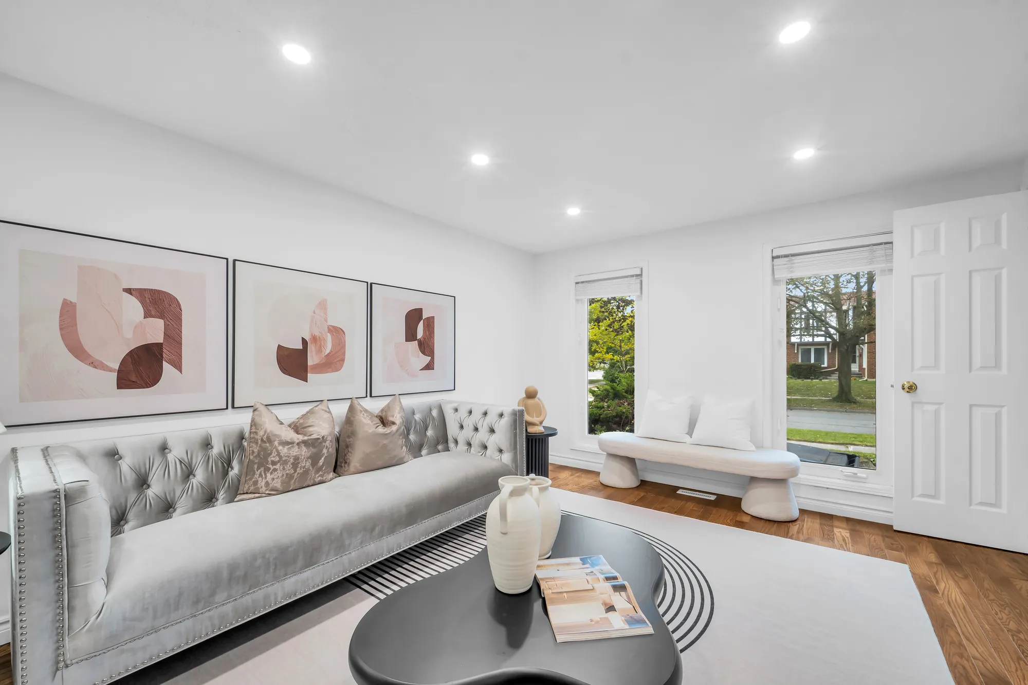 The tufted sofa under three prints, a window and a door at the far end, wood floors