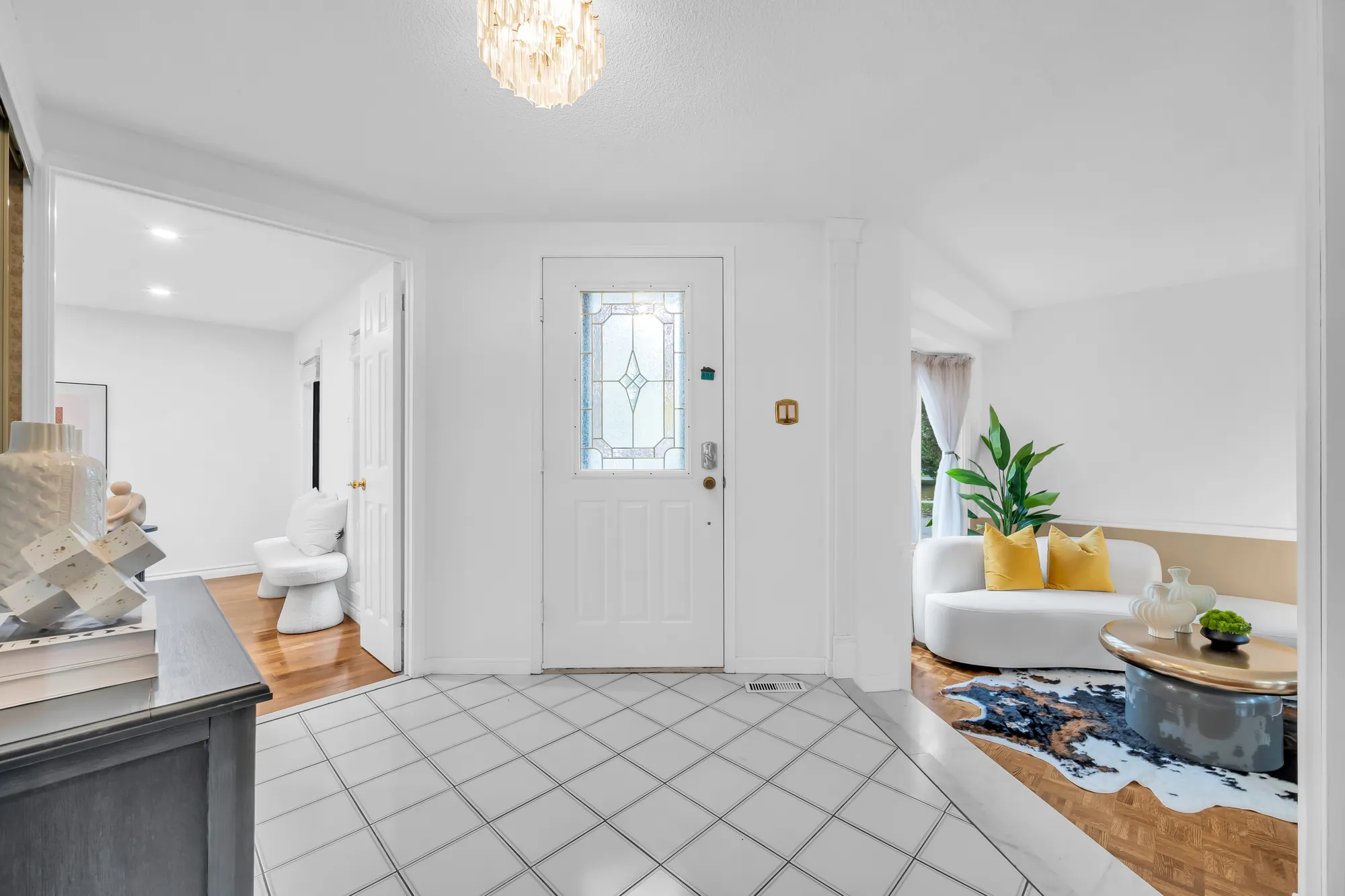 The foyer: a white front door with a leaded-glass panel, a tiled floor, a crystal light, the living room a step down at the right, a doorway at the left