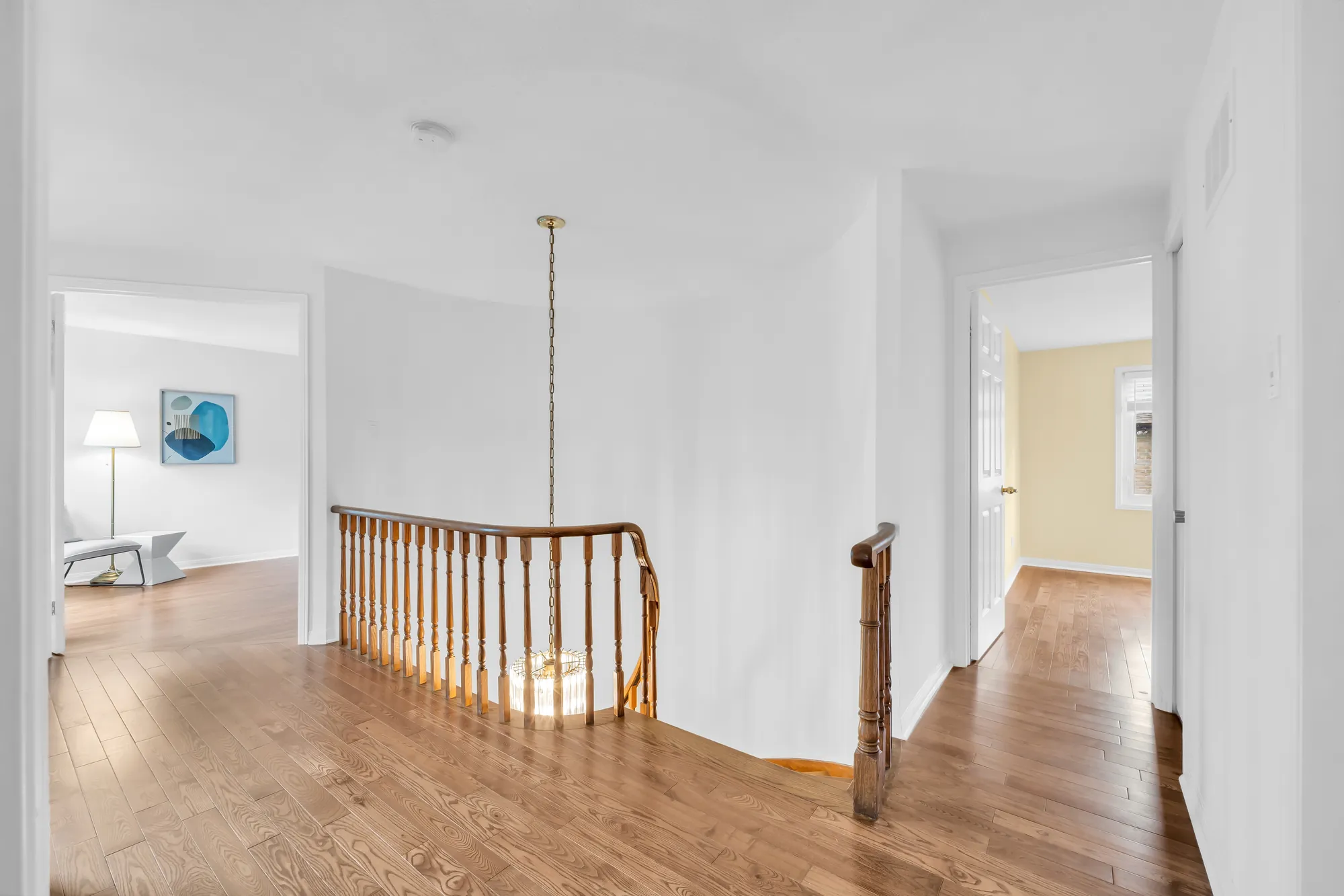 The upstairs hall: the oak railing around the stairwell, a pendant light, doors to the bedrooms, wood floors