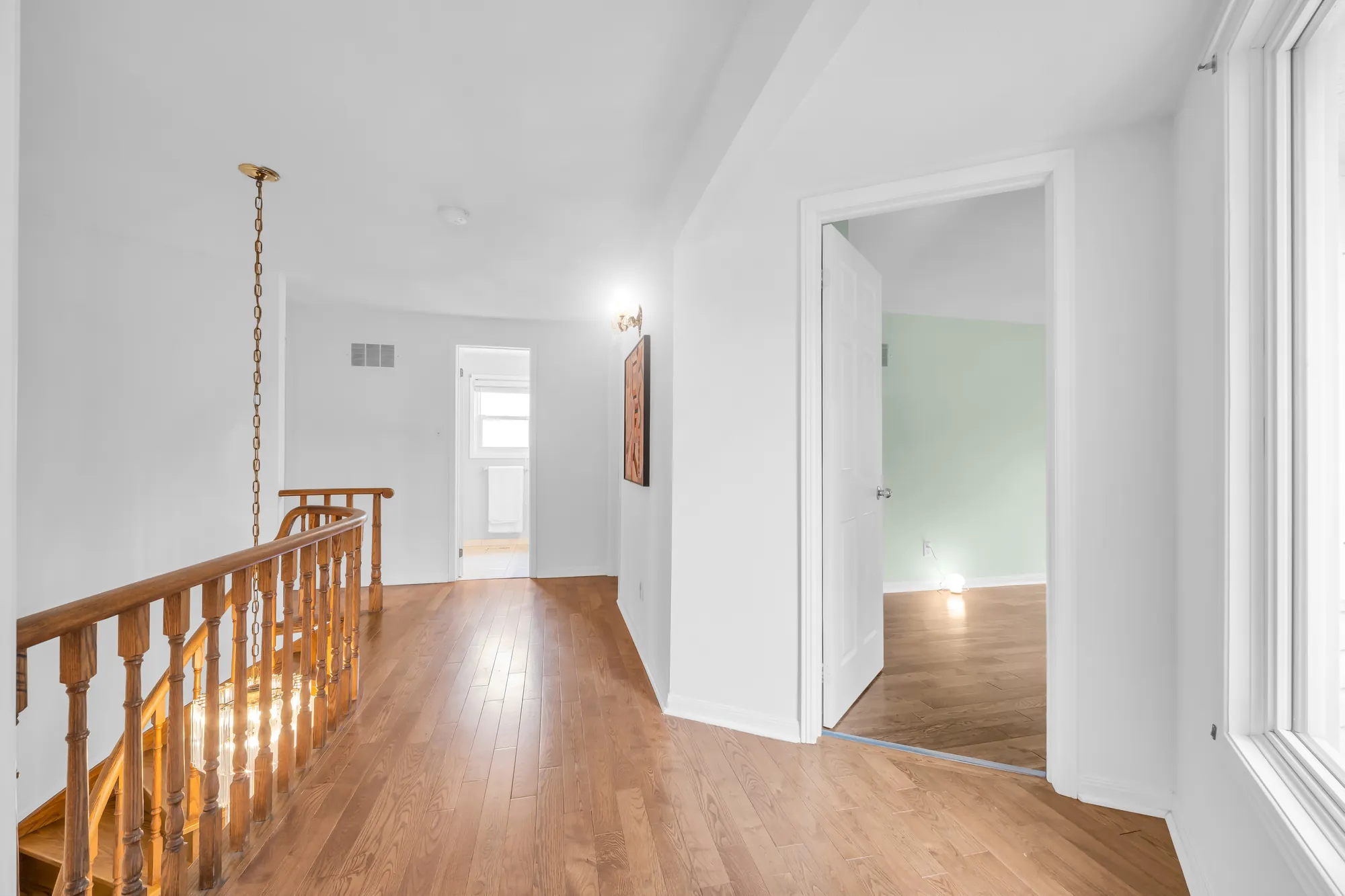 The upstairs hall toward a window at the end, the stair railing at the left, a bedroom door open at the right
