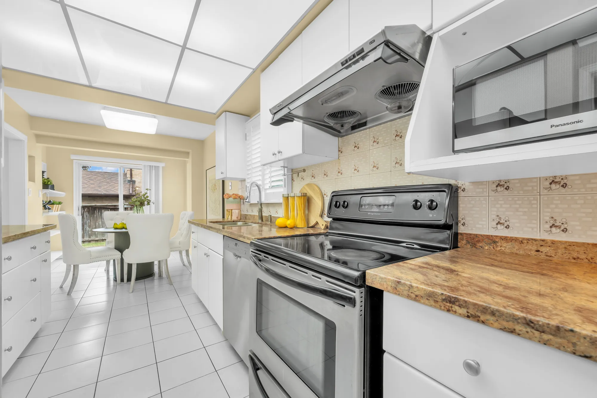 The range under a hood fan, a microwave in the cabinet beside it, the breakfast room and its sliding door beyond