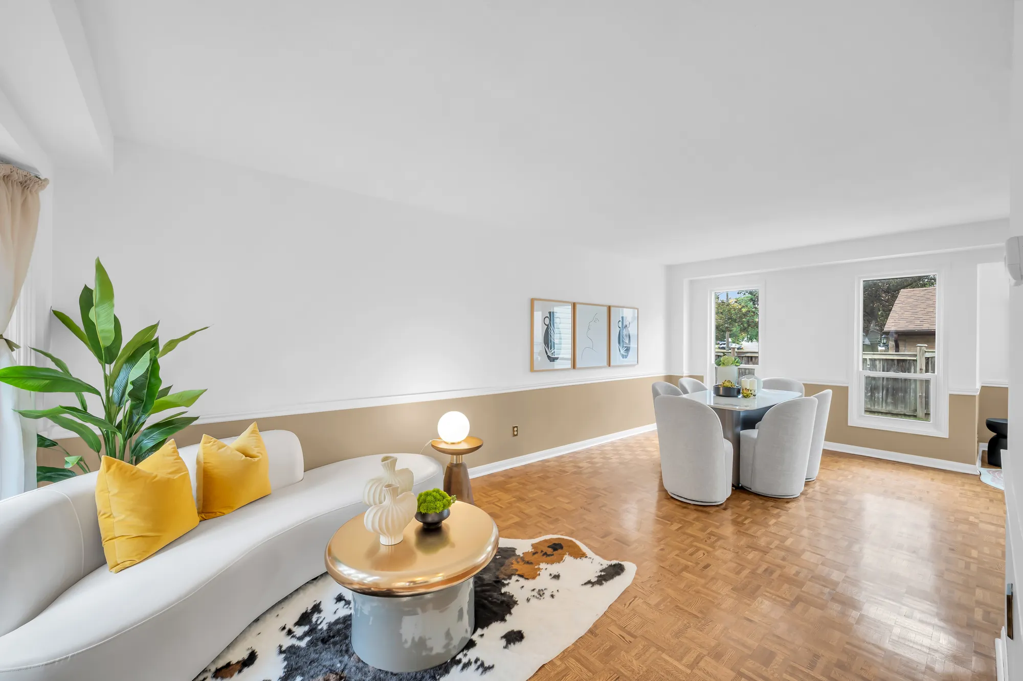 The living room: a curved white sofa on a hide rug, a round coffee table, parquet floors, a chair rail, the dining area and the back windows beyond