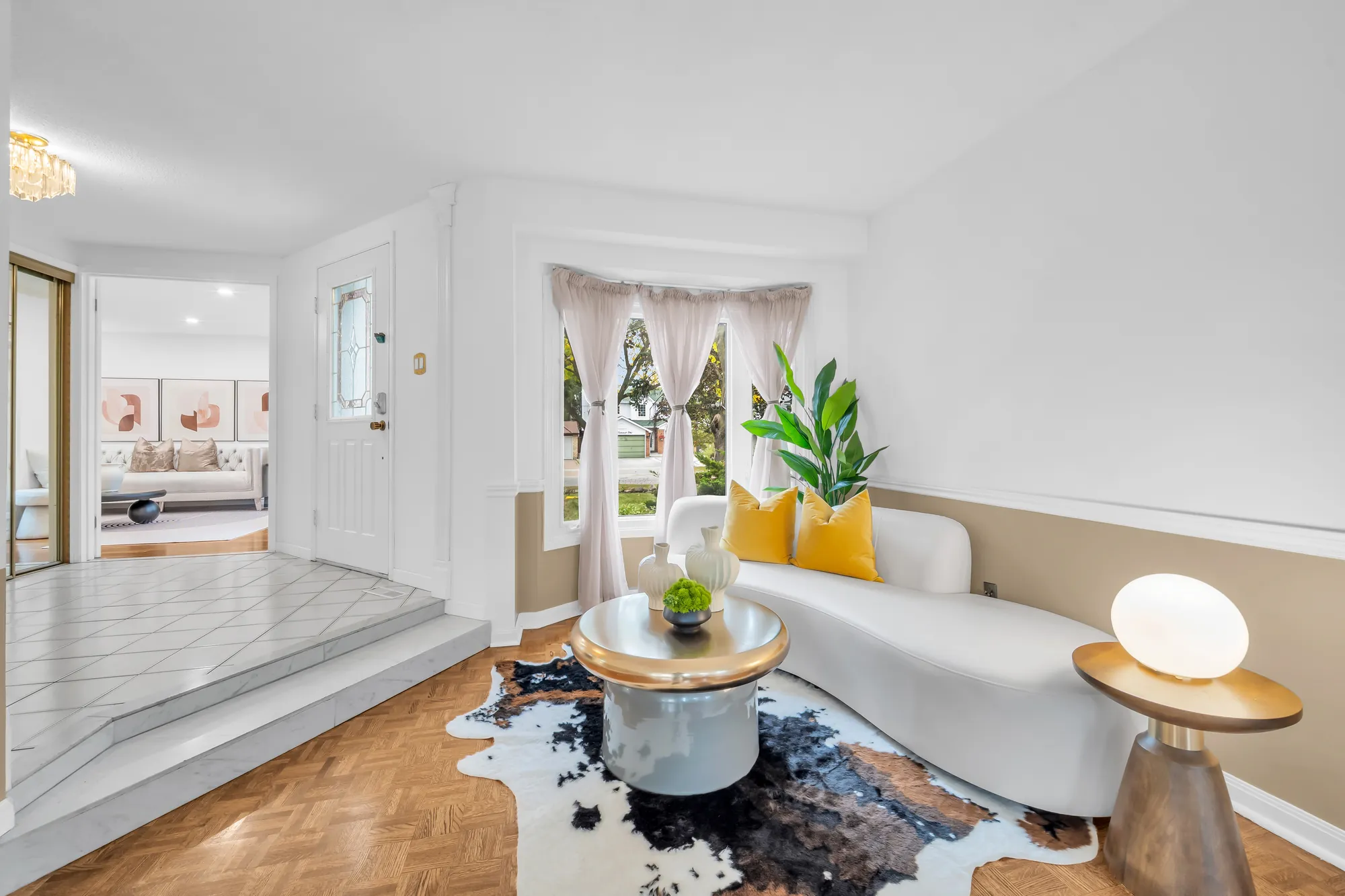 The living room toward the front: a bay window with sheer curtains, the curved sofa, a step up to the tiled foyer at the left