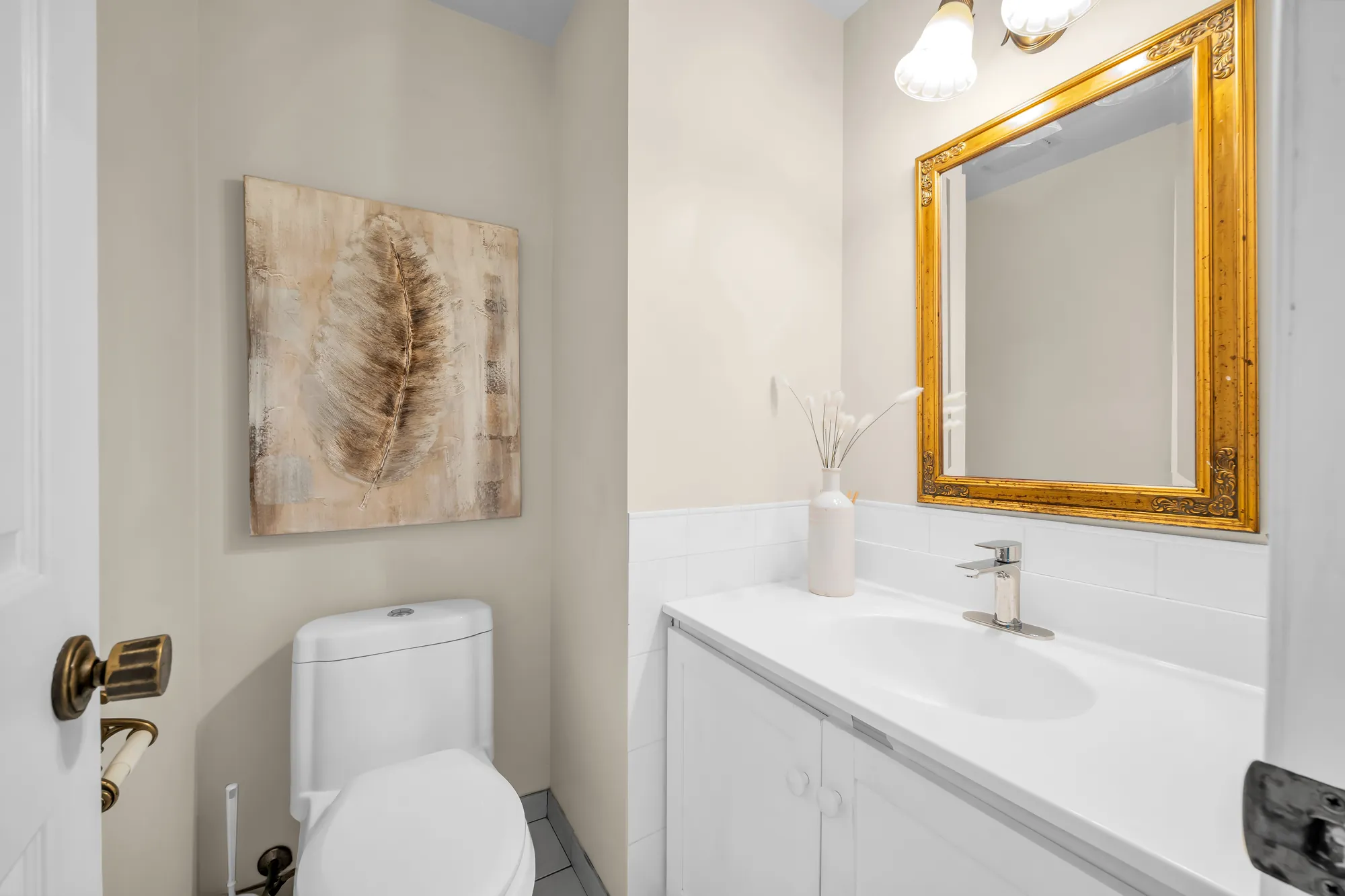 The powder room: a toilet and a white vanity, a gilt-framed mirror, a leaf print on the wall
