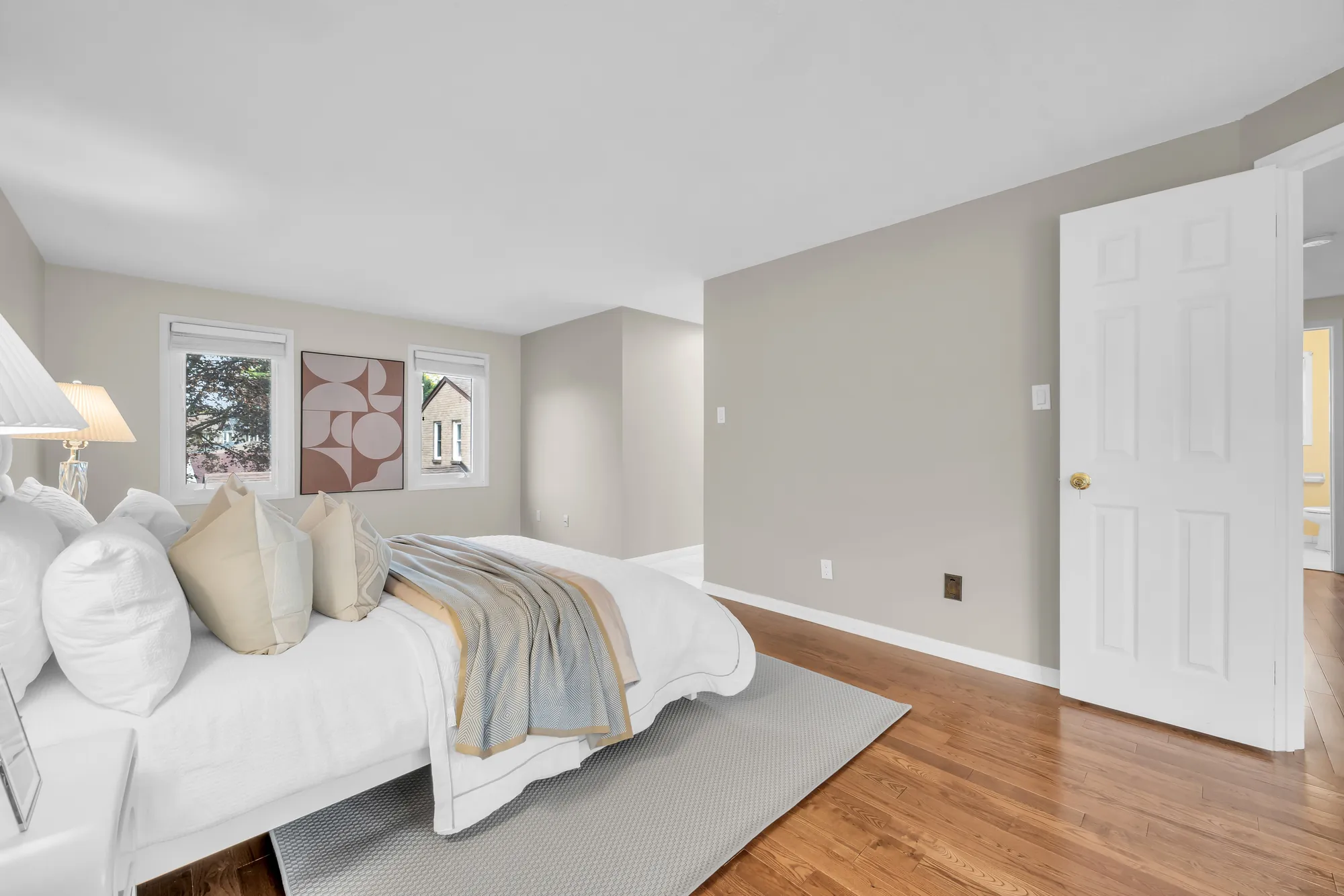 The bed from the side, the windows and a framed print beyond, a door at the right