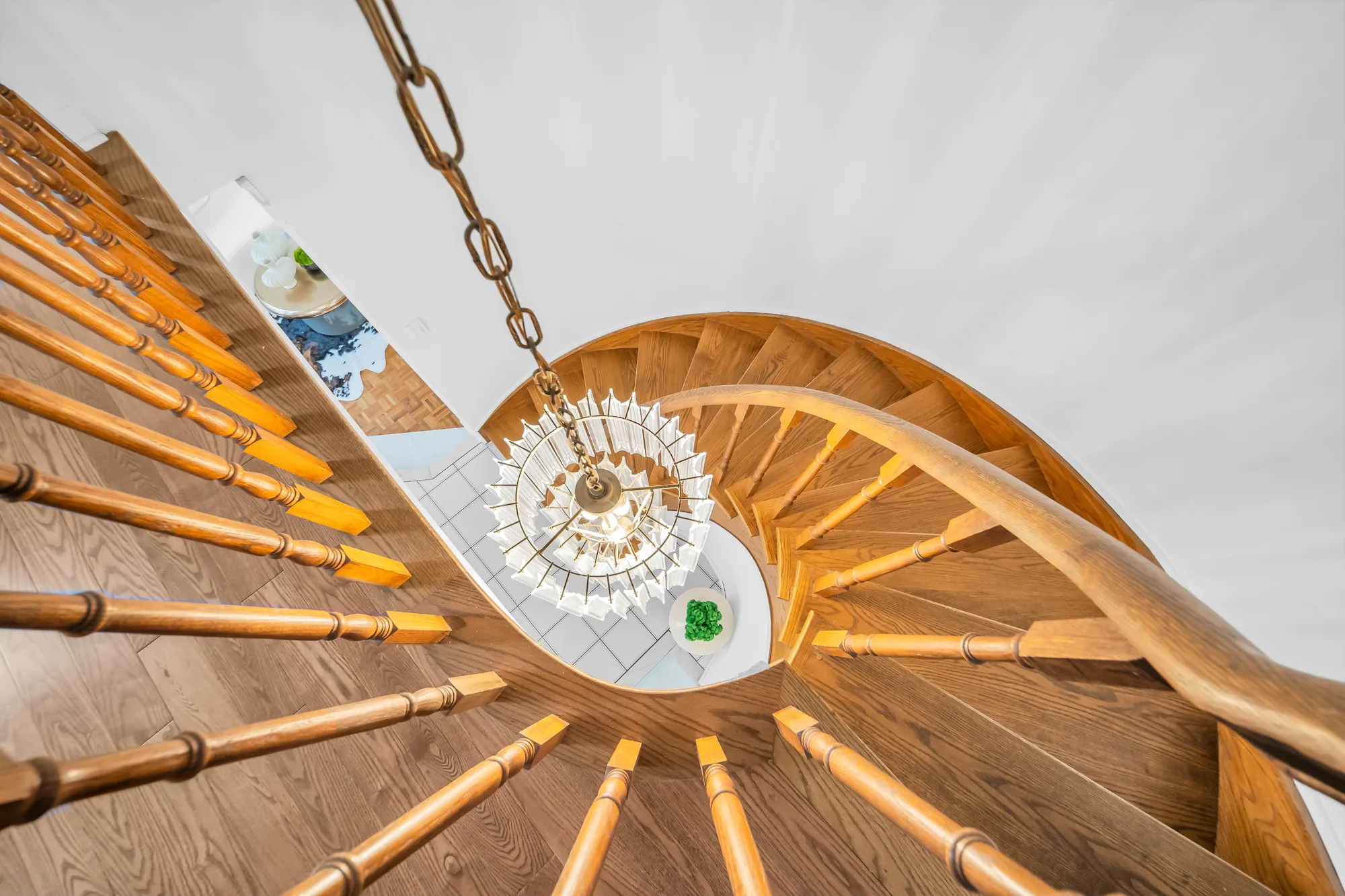 Looking up the curved oak staircase from below: the spindles and the handrail spiralling around a crystal chandelier
