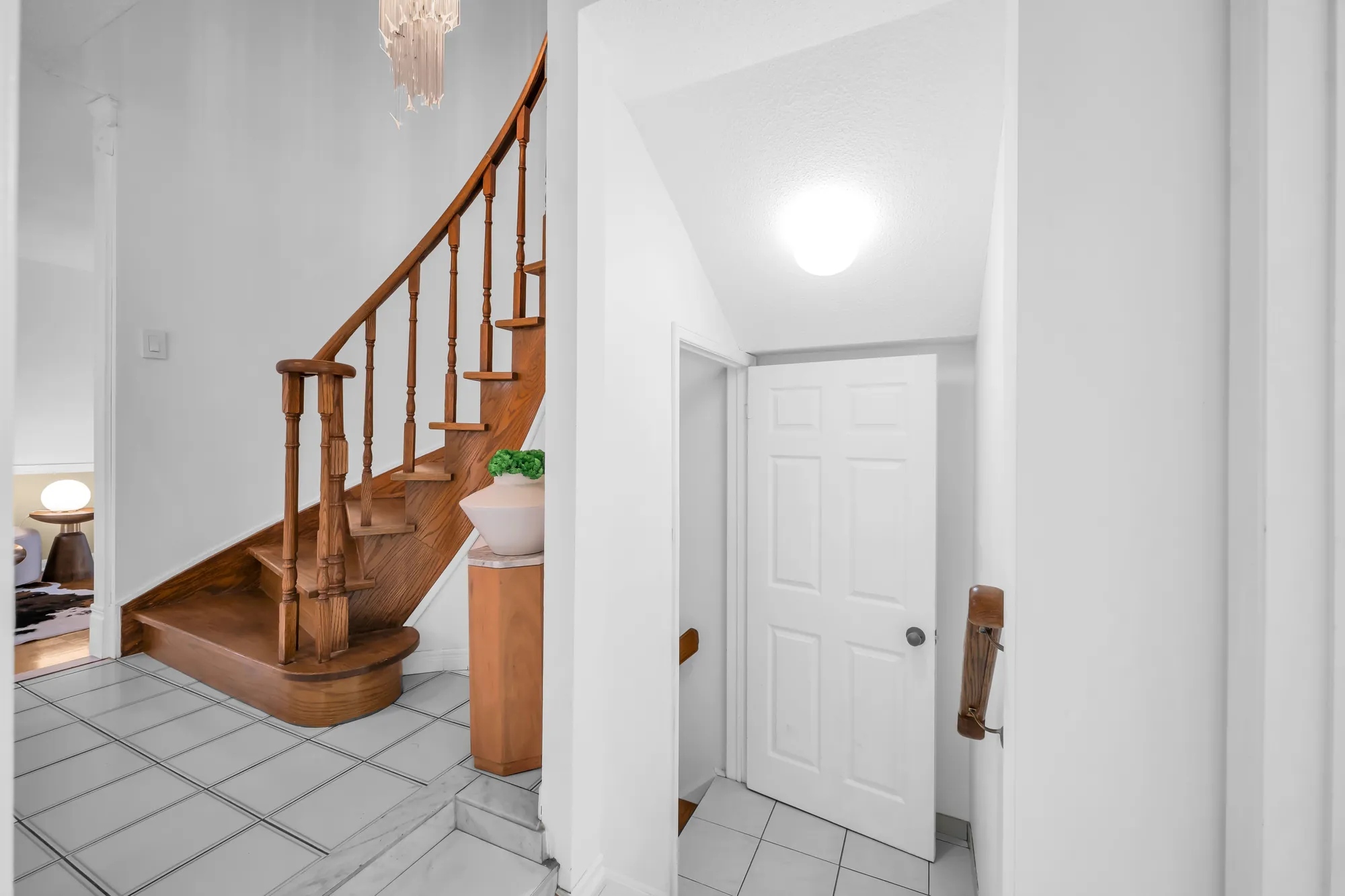 The foot of the staircase from the hall, its oak treads and turned spindles, a closed door at the right