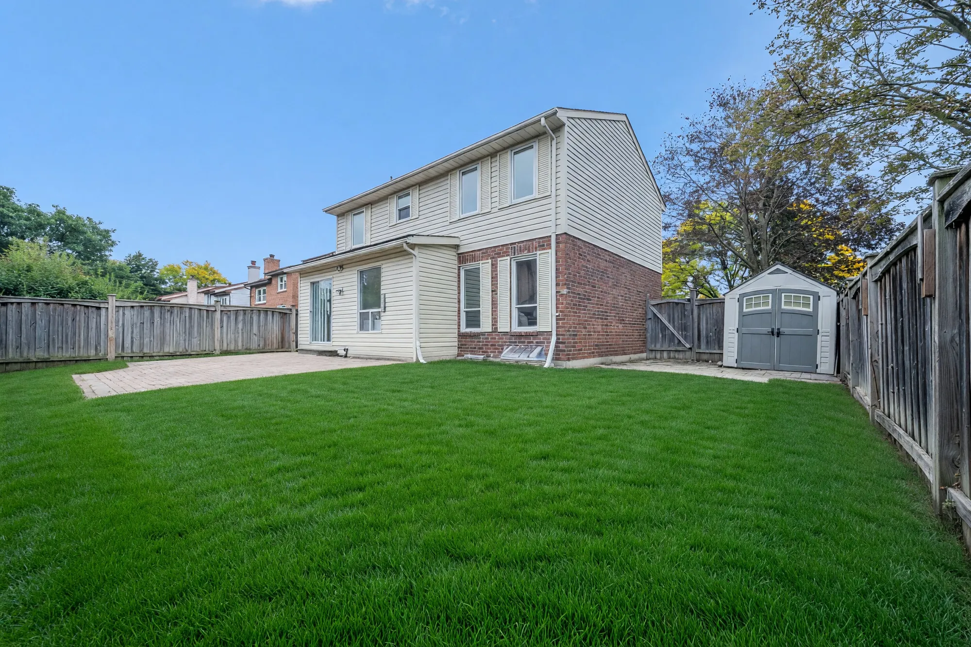 The back yard: a lawn along a wooden fence, the back of the house with its sliding door, a patio, a garden shed in the corner